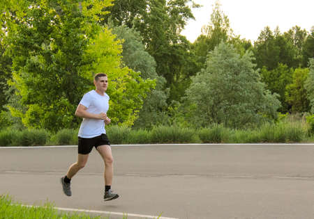 A guy runs in the summer on an asphalt road, doing sportsの写真素材