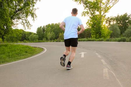A guy runs in the summer on an asphalt road, doing sportsの写真素材