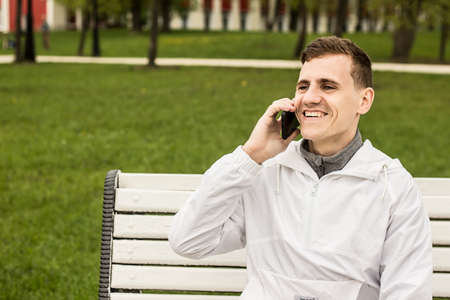 Young handsome businessman talking on mobile phone while sitting on a bench in parkの写真素材