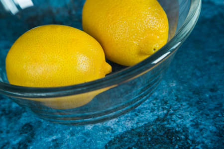 Fresh yellow lemons in a glass bowl on a blue background.の写真素材