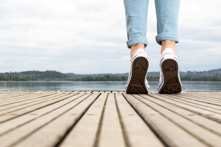 Legs of a young girl on tiptoe on a wooden pier with white shoes in front to the lakeの写真素材