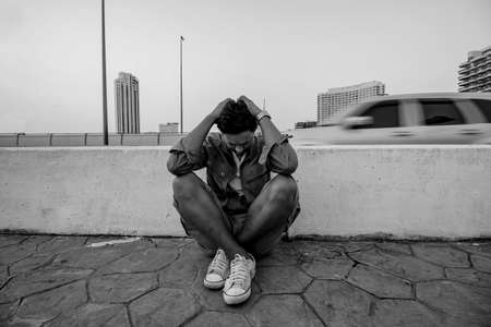 Asian young man with depression sitting beside street in a big city.の写真素材