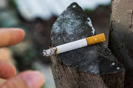 Hand and a cigarette on a wooden background. Addiction concept