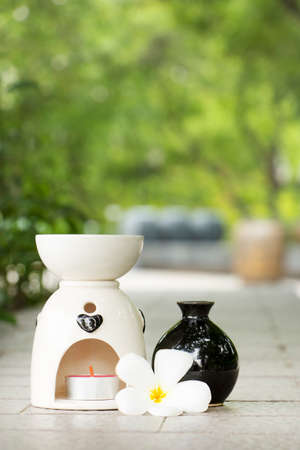 Aromatherapy oil burner with aromatherapy candles and frangipani flower. Spa concept in the garden.