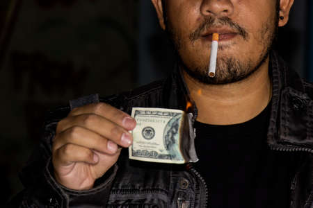 Handsome man lighting his cigar with dollar note. Concept idea.