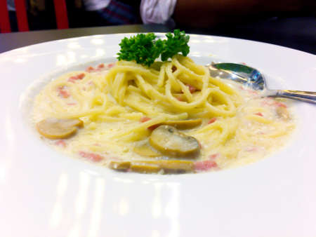 Spaghetti with hams, mushroom and cheese sauce is decorated with parsley leaves that is in white dish with silver spoon.の写真素材