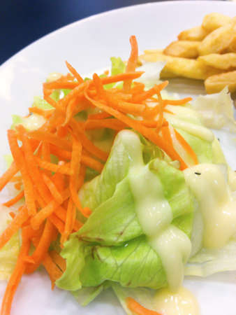 Colorful vegetable salad topped with mayonnaise and french freis that are on the white plate.の写真素材