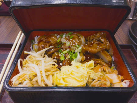 Japanese food set, stir-fried pork with soy sauce, sprinkled with white sesame seeds and onions, topped with rice. And side dishes are fried bean sprouts, omelet cut into strips and kimchi. All of these are served in traditional Japanese rice box.の写真素材