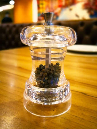 Black pepper in transparent bottle for grinding, it is on the wooden table. Selective focus. Focus on foreground and copy space.の写真素材