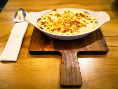 Baked spinach with cheese that is in  white bowl, it is on wooden table in the restaurant. Selective focus and copy space.の写真素材
