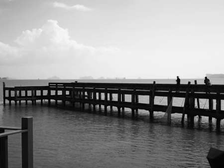 The concept of hopeless living on the coast background. Villagers are catching fish by using fishing net at the dock, which extends into the emerald sea on a foggy day. Selective focus and copy space.の写真素材
