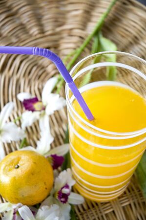 glass of juice put beside an orange and orchidの写真素材