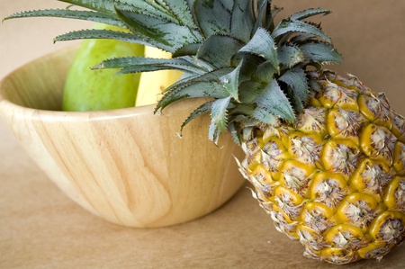 fresh pineapple put beside wooden bowl