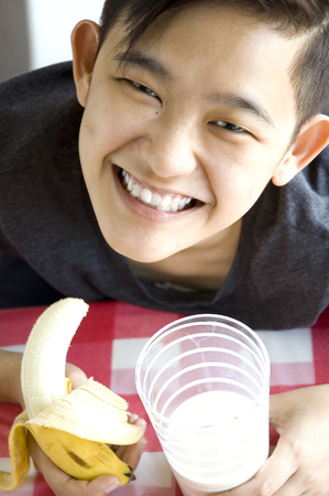 young asian holding glass of milk and banana for breakfastの写真素材