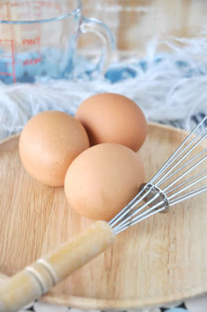 eggs and whisk put on wooden plate with measuring cup on background