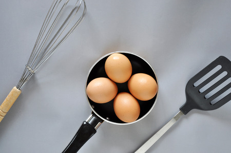 Eggs in pan with utensil on gray backgroundの写真素材
