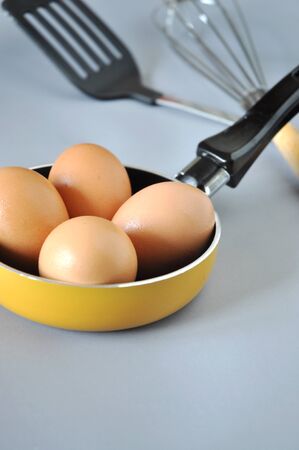 Four raw eggs in yellow pan with utensil on backgroundの写真素材