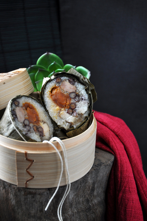 Zongzi Chinese food in bamboo steam container put on wooden with red and black backgroundの写真素材