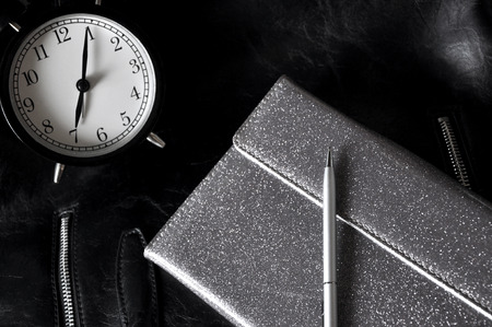 Black alarm clock with silver organizer notebook on black leather background