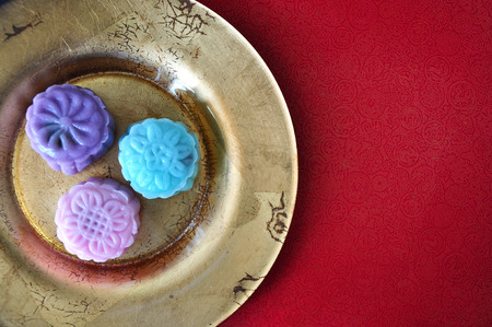 Top view of colorful snowy mooncake on golden plate put on red background with space for textの写真素材