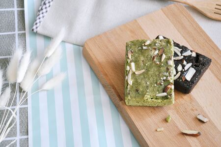 Matcha green tea brownie and dark chocolate brownie on wooden board decorated with white flowers put...