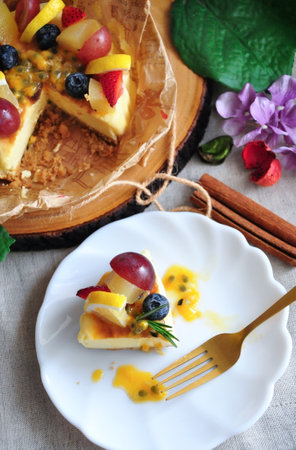 Above of a piece of New York cheesecake topping with summer fruits and passion fruit sauce serving on white dish with golden forkの写真素材