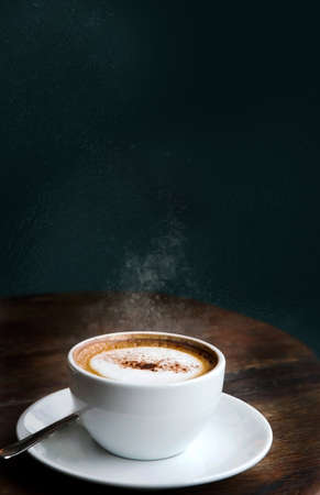 A cup of hot cappuccino on wooden table with space for text on dark green backgroundの写真素材
