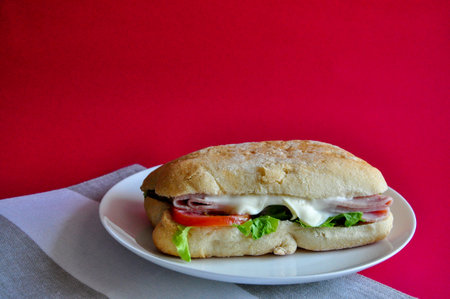 Fresh ham cheese sandwich on white dish with copysapce on red backgroundの写真素材