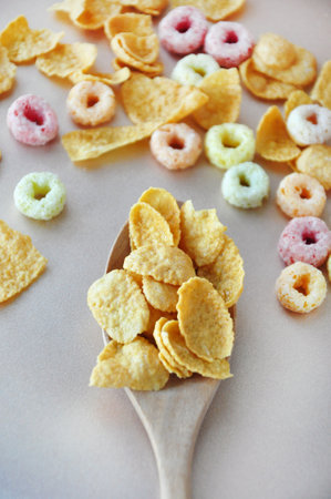 Top view of corn flakes cereal in wooden spoon with fruit loops cereal on background