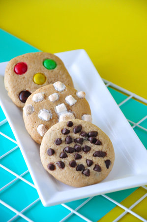 Variety soft cookies chocolate chip, marshmallow and colorful chocolate candy on white plate with...