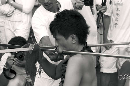 PHUKET, THAILAND OCTOBER 2 2011: A Ma Song (vessel of the gods) at the Bang Niew Chinese Shrine in Phuket Town pierces his face with two heavy metal rods during a ritual ceremony at the annual Phuket Vegetarian Festival.のeditorial素材