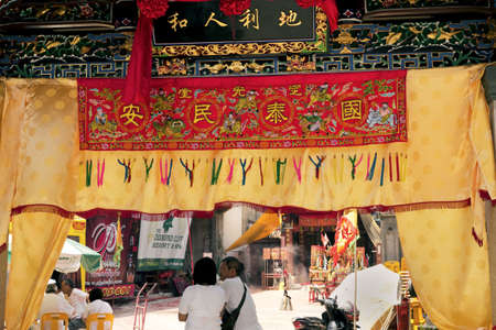 PHUKET, THAILAND OCTOBER 2 2011: A man and woman in in ceremonial white walk under a banner gate at the Shrine of Serene Light during the annual Phuket Vegetarian Festival in Phuket Town.のeditorial素材