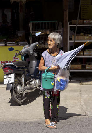 PHUKET, THAILAND SEPTEMBER 6 2011: An elderly worshiper in Phuket Town waits for traffic before crossing the street to the Put Jaw Chinese Temple for prayer. のeditorial素材