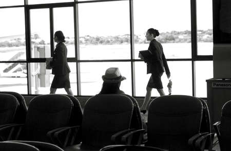 UDON THANI, THAILAND JULY 19 2012: Two airline reps walk by a Thai woman waiting for a departing...