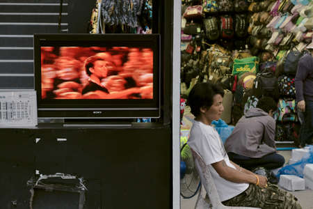 PHUKET, THAILAND APRIL 30 2012: A street peddler hawks his wares next to a wide screen TV along...