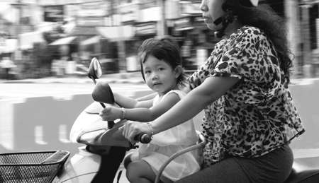 PATONG, PHUKET, THAILAND MAY 7 2012 A toddler rides in front of her mom on a moped as she crosses the intersection of Rai-tu-Thit and Sainamyen Roads in Patong. のeditorial素材