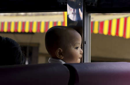 PHUKET, THAILAND SEPTEMBER 6 2011: A little Burmese boy fresh from his bath (talcum powder on  face) gazes out an open window as he rides a public bus through Phuket Town.のeditorial素材