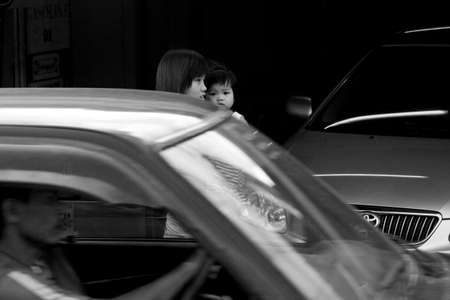 PATONG, PHUKET, THAILAND JULY 22 2012: A mother carrying her daughter waits for passing traffic before crossing Sainamyen Road in Patong Beach.のeditorial素材