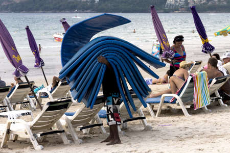 PATONG BEACH, PHUKET, THAILAND NOVEMBER 16 2012: A Thai beach vendor flips sun lounger cushions on Patong Beach.のeditorial素材