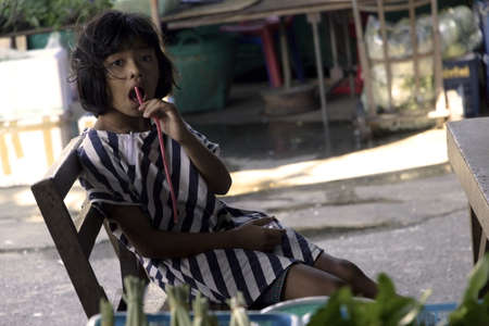 PHUKET THAILAND APRIL 19 2013: Young Thai girl munches on a piece of licorice at her parents vending stall at the Downtown Market in Phuket Townのeditorial素材