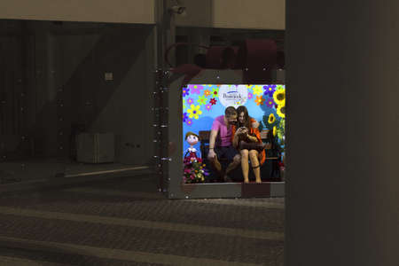 JUNCEYLON MEGAMALL, PATONG, PHUKET, THAILAND JANUARY 2 2013: A couple on holiday sits inside a boxed promotional display while looking at photos on their mobile camera phone. のeditorial素材