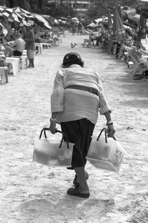PATONG BEACH, PHUKET, THAILAND DECEMBER 11 2010: An elderly beach peddler sells beverages and snacks on Patong Beach.のeditorial素材