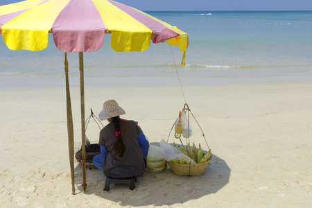 KAMALA BEACH, PHUKET, THAILAND JANUARY 26 2013: Vendor selling corn-on-the-cob does business from under a large beach umbrella to avoid the hot sun.のeditorial素材