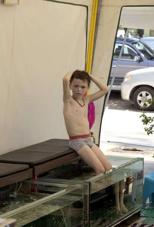 KAMALA BEACH, PHUKET, THAILAND - JANUARY 13 2013: A young Russian boy cools off with a fish pedicure at Kamala Beach during the high season in Phuket.のeditorial素材