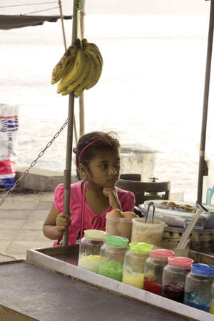 KALIM BEACH, PHUKET, THAILAND JANUARY 20 2013: The daugher of a snack vendor plays beside her parents\' concession stand.のeditorial素材