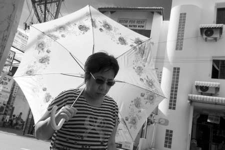 SAINAMYEN ROAD, PATONG, PHUKET, THAILAND JULY 25 2012: A Thai woman walking in Patong Beach shields herself from the hot sun with an umbrella.のeditorial素材