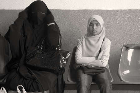 GENTING HIGHLANDS, MALAYSIA OCTOBER 16 2009: A Muslim woman in full burqa sits next to a Malaysian child in a hijab at a bus depot in Genting Highlands. のeditorial素材