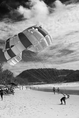 PATONG BEACH, PHUKET, THAILAND, AUGUST 3 2011: A parasail rental operator pulls in an open canopy after a ride.のeditorial素材