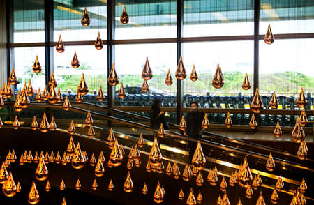 CHANGI AIRPORT, SINGAPORE, 20 MAY 2014:  Two passengers ride an escalator past Kinetic Rain, a large, moving kinetic art sculpture. The largest of its kind in the world, Kinetic Rain hangs inside the departure hall at Singaporeのeditorial素材