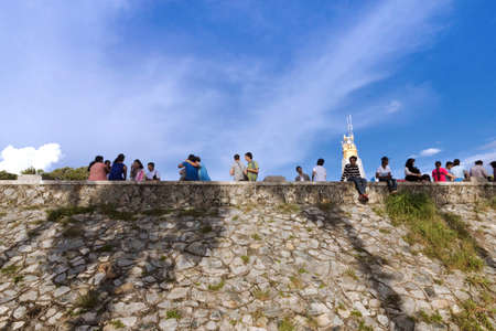CAPE PROMTHEP, THE TIP OF PHUKET ISLAND, THAILAND, 17 AUGUST 2014: Row of tourists sit and rest on a wall whilst visiting Cape Promthep, one of the most scenic vistas the resort island of Phuket has to offer.のeditorial素材